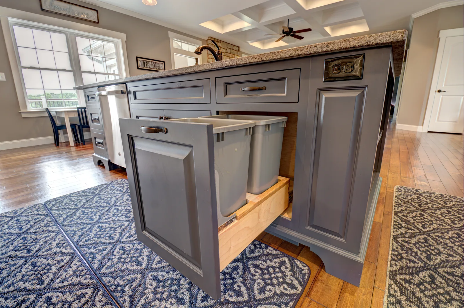 Custom gray kitchen island under a coffered ceiling with white perimeter cabinetry